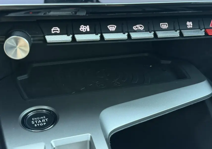 Vue rapprochée de la console centrale du Peugeot 308 Hybrid 2025, montrant le bouton start/stop et le chargeur induction.