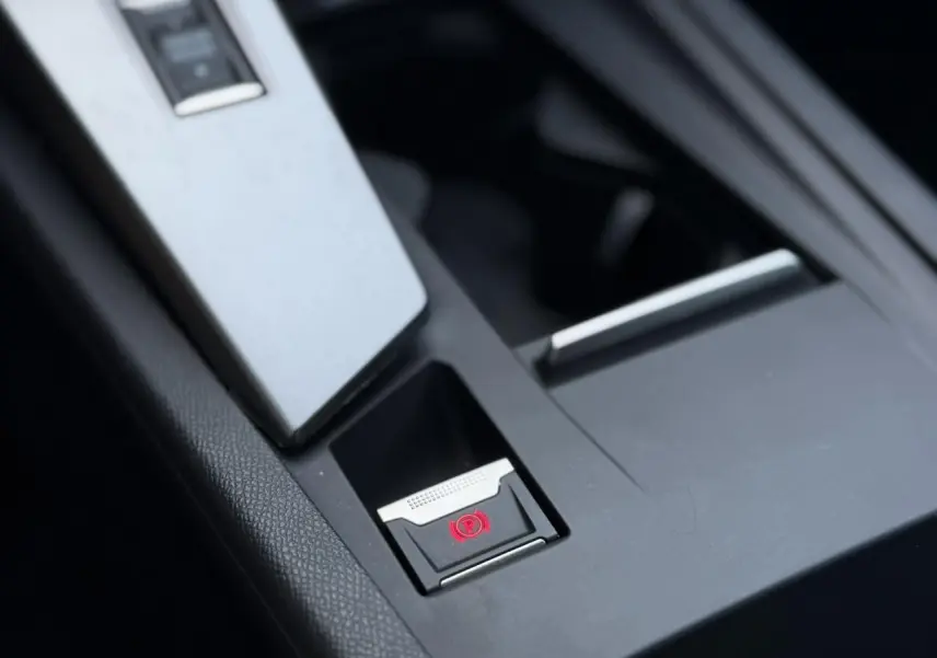 Gros plan sur le frein de parking électrique rouge dans la console centrale noire du Peugeot 308 Hybrid 2025.
