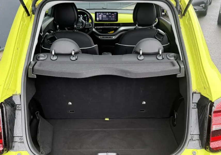 Vue arrière du coffre ouvert d'une FIAT 500 électrique jaune Acid, avec intérieur noir et tableau de bord visible.