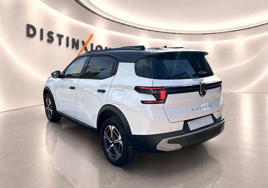 Vue 3/4 arrière droite d'un Citroën C3 Aircross blanc avec toit noir et jantes alu en intérieur showroom.