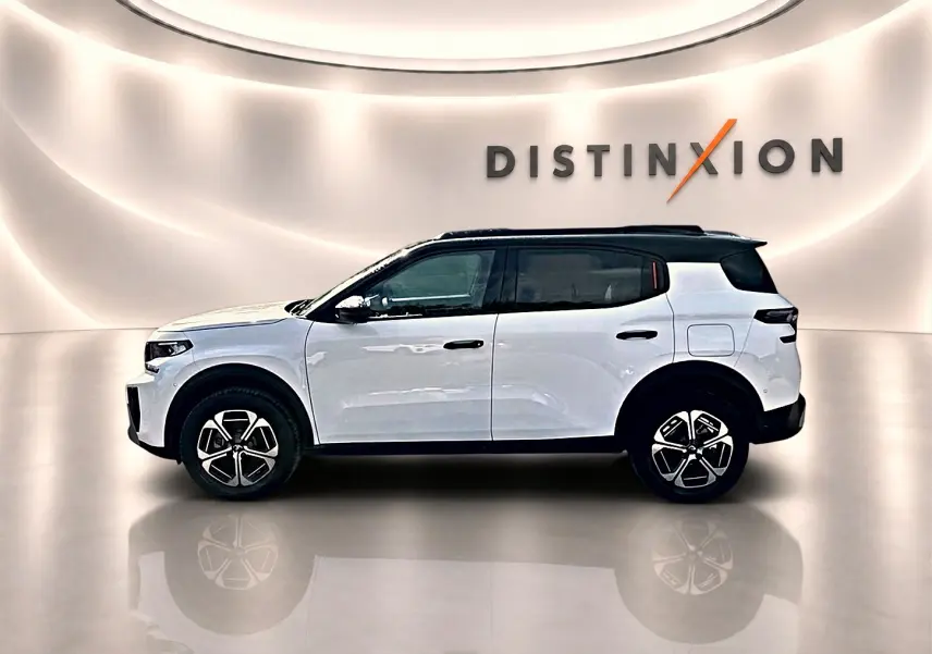 Profil droit d'un Citroën C3 Aircross blanc avec toit noir, jantes alu et vitres arrière teintées dans un showroom lumineux.