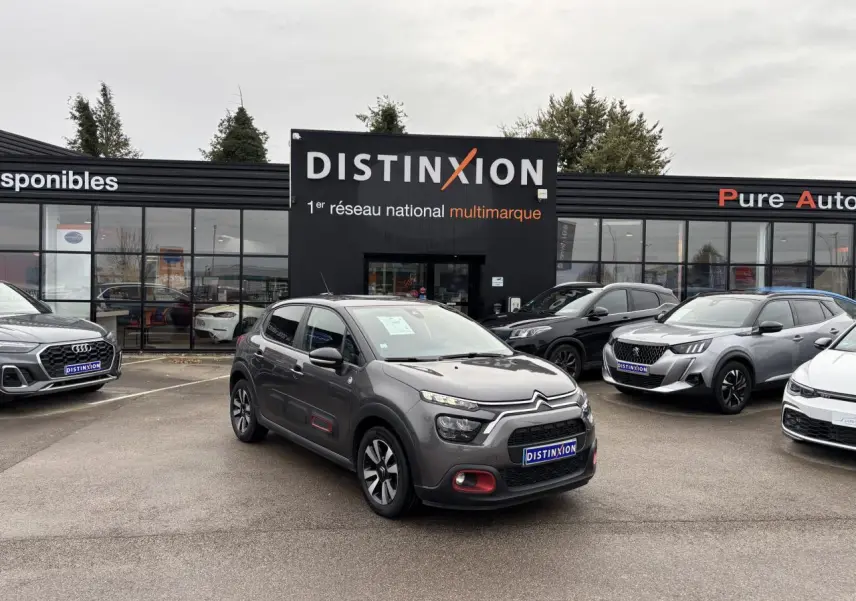 Citroën C3 gris foncé vue 3/4 avant droit avec décorations rouges sur les portes, stationnée devant un concessionnaire Distinxion.