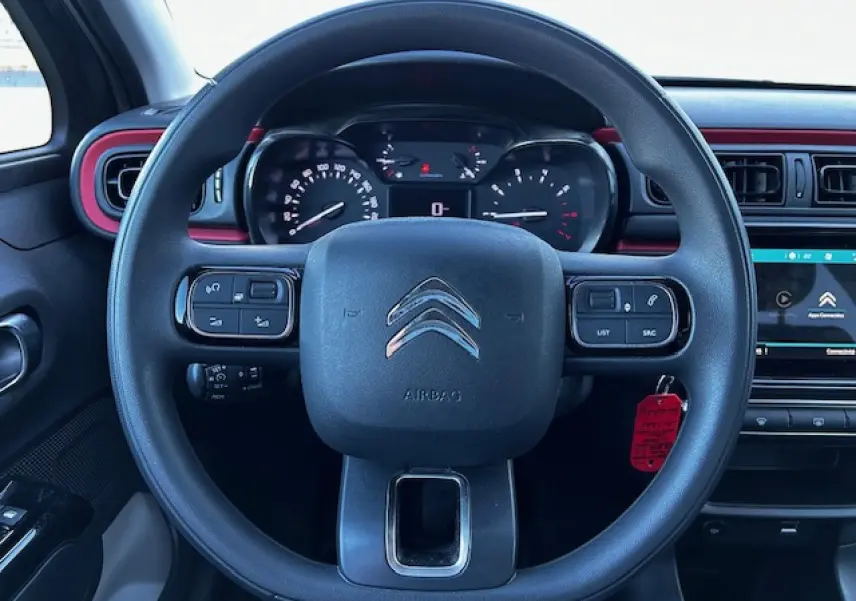 Vue frontale du volant noir de la Citroën C3 III 1.2 PureTech avec tableau de bord et écran tactile rouge et noir.