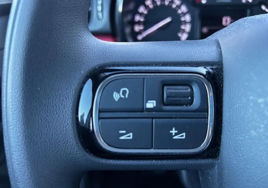 Gros plan sur les commandes audio au volant noir de la Citroën C3 III gris foncé, avec tableau de bord flou en arrière-plan.