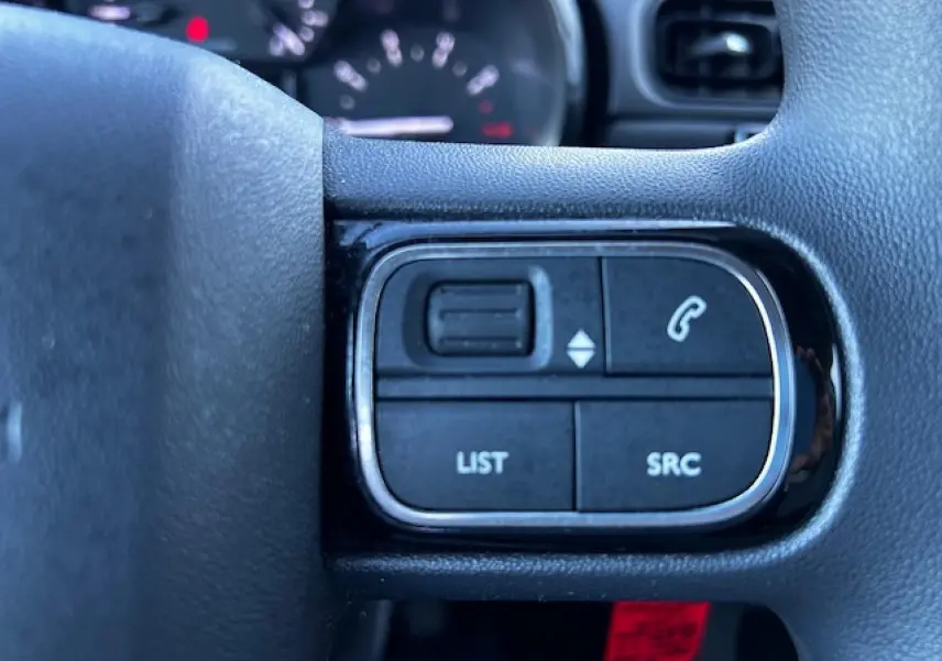 Gros plan sur les commandes audio au volant noir de la Citroën C3 III gris foncé, avec boutons list et appel.