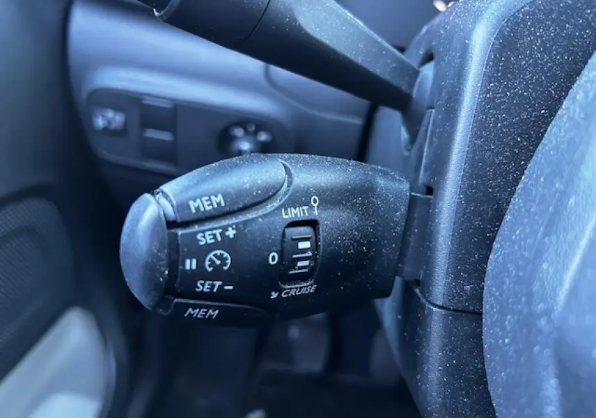 Gros plan sur la commande de régulateur de vitesse noire à gauche du volant dans une Citroën C3 gris foncé.