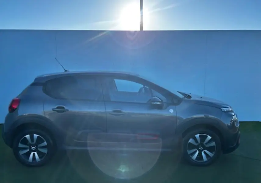 Profil côté gauche d'une Citroën C3 gris foncé 2021 avec enjoliveurs noirs et détails rouges sur les portes