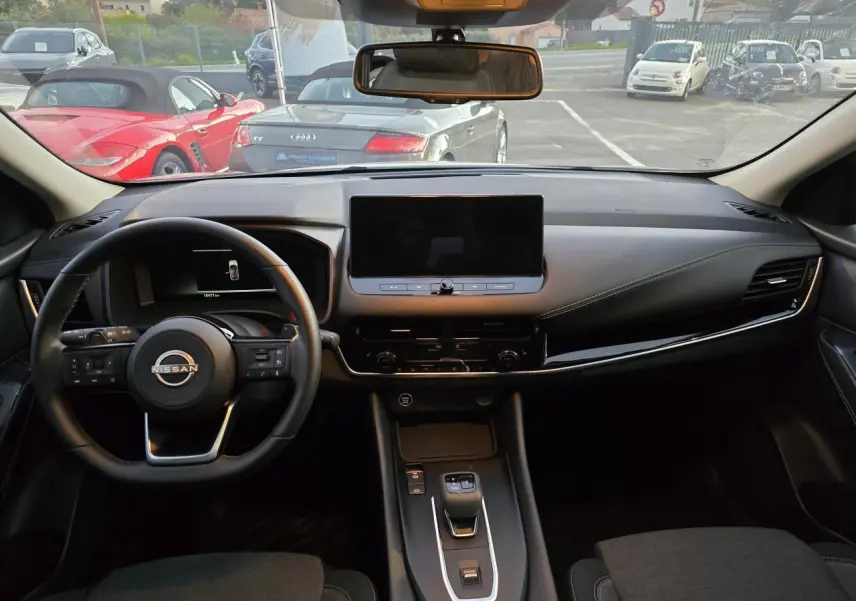 Vue intérieure avant du Nissan Qashqai gris silver 2024, tableau de bord moderne avec écran tactile central et volant cuir.