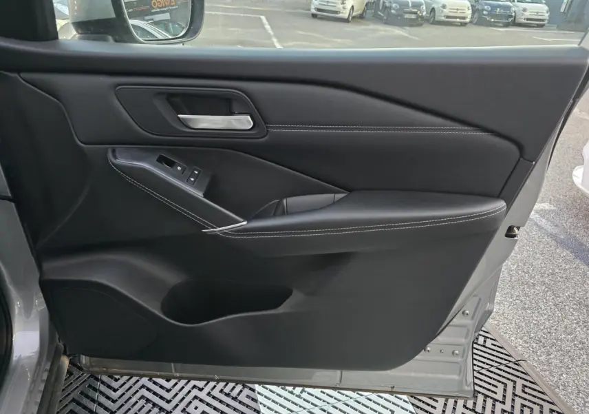 Porte intérieure côté gauche du Nissan Qashqai gris silver 2024, avec garniture noire et surpiqûres blanches visibles.