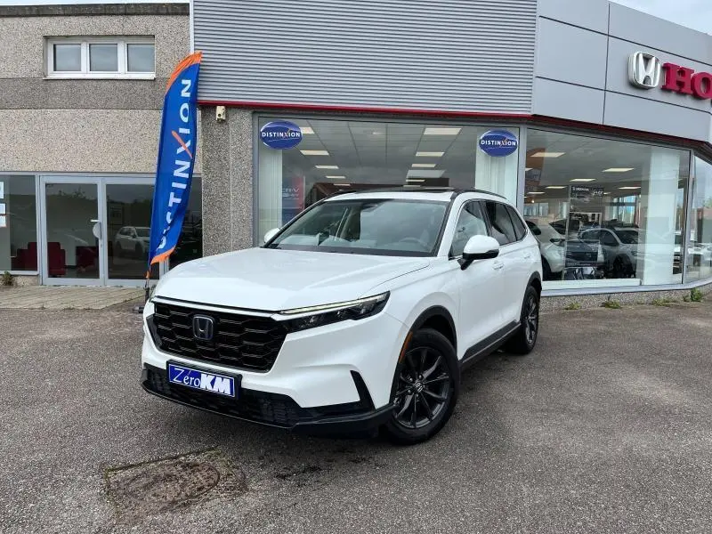 Vue 3/4 avant d'un Honda CR-V blanc platine nacré garé devant un concessionnaire avec jantes noires et toit panoramique.