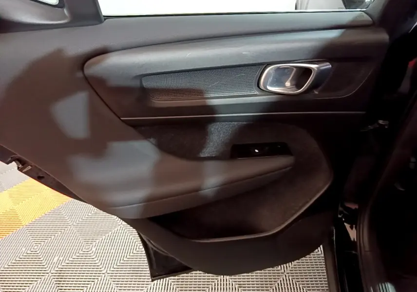 Gros plan sur la porte arrière gauche noire du Volvo XC40 Recharge T4 avec poignée chromée et commande de vitre.