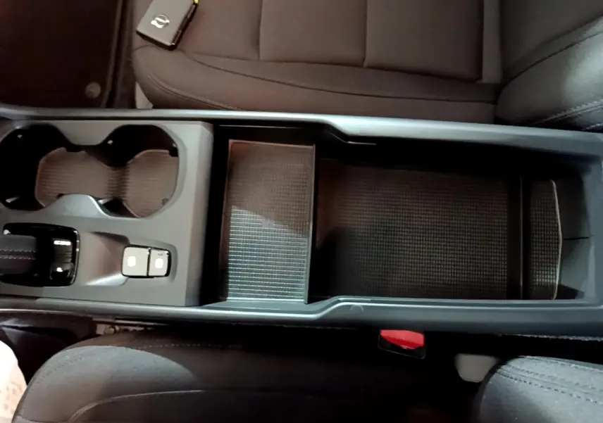 Vue plongeante sur la console centrale noire du Volvo XC40 Recharge T4 avec porte-gobelets et accoudoir ouvert.