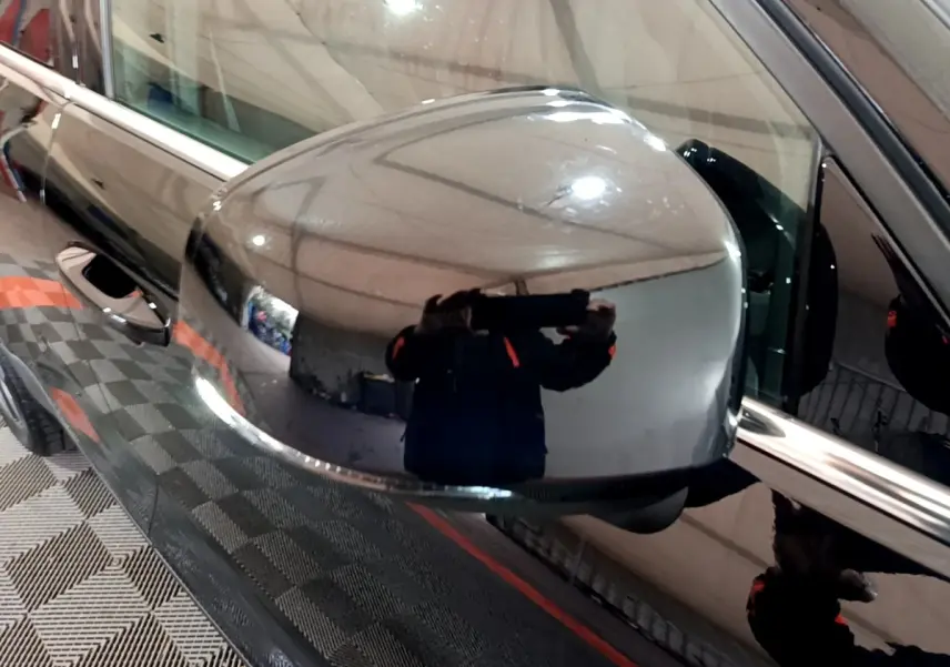 Rétroviseur côté gauche noir brillant du Volvo XC40 Recharge T4 Business, reflet d'un intérieur d'atelier visible.