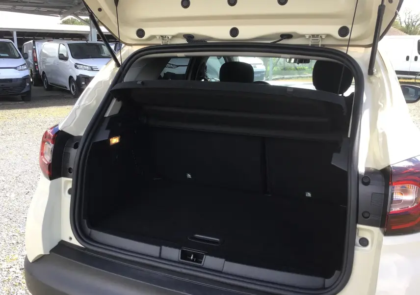 Coffre ouvert vu de l'arrière d'un Renault Captur beige/marron, montrant l'espace de chargement vide et la plage arrière.