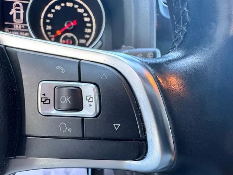 Gros plan sur les commandes multifonctions gauche du volant cuir noir du Volkswagen Scirocco 1.4 TSI 2017, avec tableau de bord en arrière-plan.