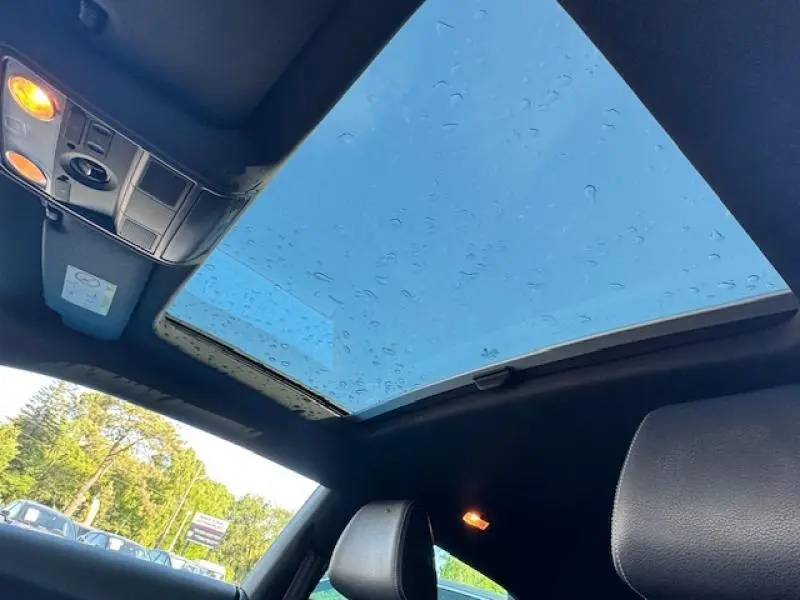Vue intérieure du toit panoramique électrique de la Volkswagen Scirocco noire avec ciel bleu visible et éclairage intérieur allumé.