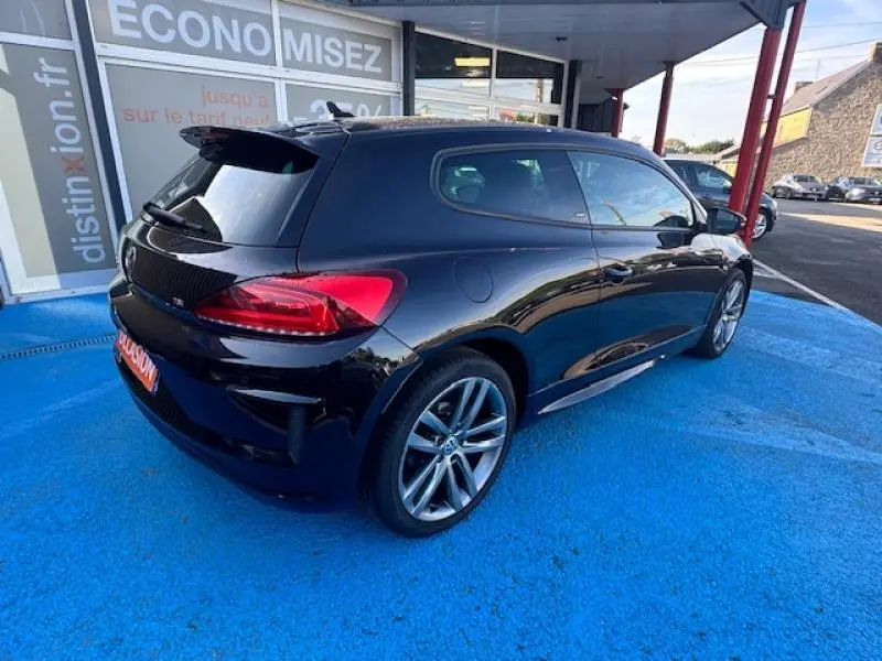Volkswagen Scirocco noir intense vue 3/4 arrière droit, jantes alu et becquet arrière visibles.
