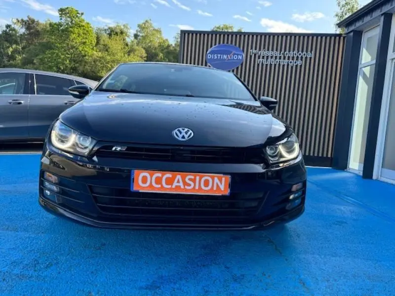 Vue avant d'une Volkswagen Scirocco noire intense avec phares allumés et plaque "OCCASION" orange.