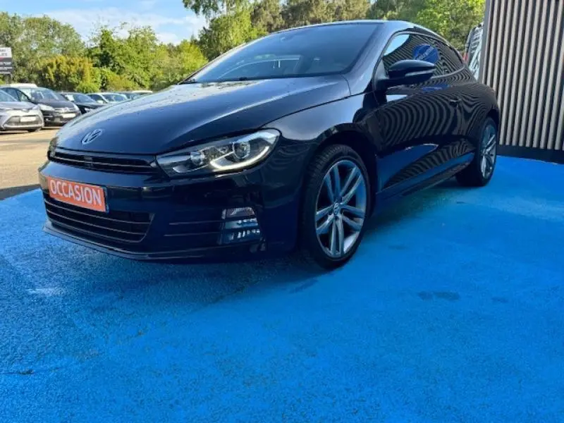 Volkswagen Scirocco noir intense en 3/4 avant droit, avec jantes alu et toit panoramique visible.