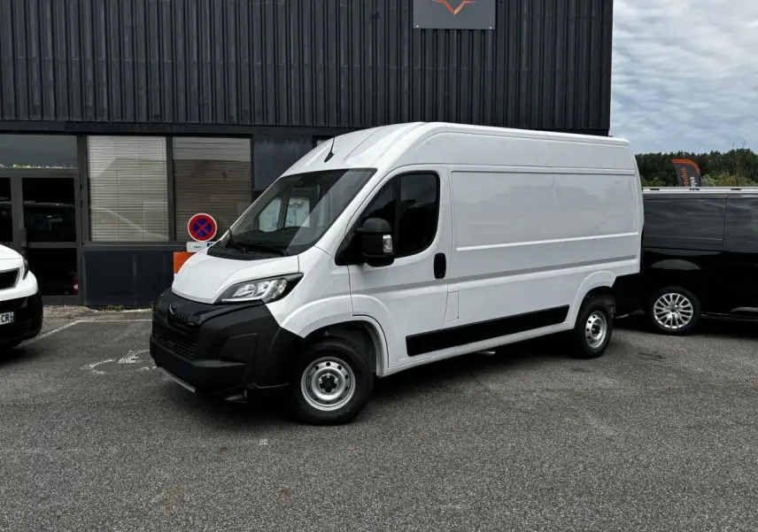Vue 3/4 avant droite d’un Peugeot Boxer Fourgon blanc avec pare-chocs noir et jantes acier, stationné devant un bâtiment.