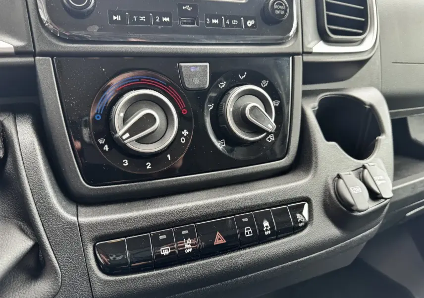 Gros plan sur la console centrale noire du Peugeot Boxer Fourgon 2026, montrant les commandes de climatisation et les prises USB et 12V.