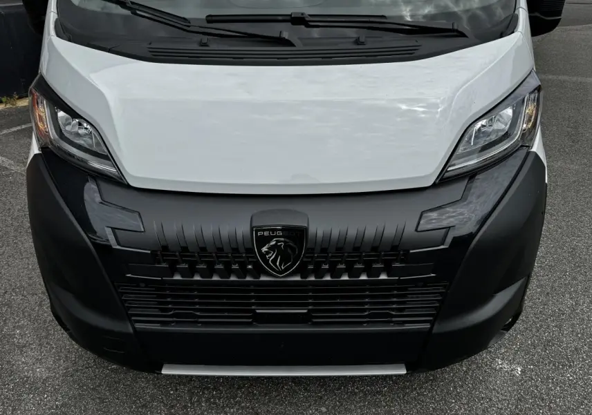 Vue frontale rapprochée du Peugeot Boxer Fourgon blanc avec calandre noire et logo lion central visible.