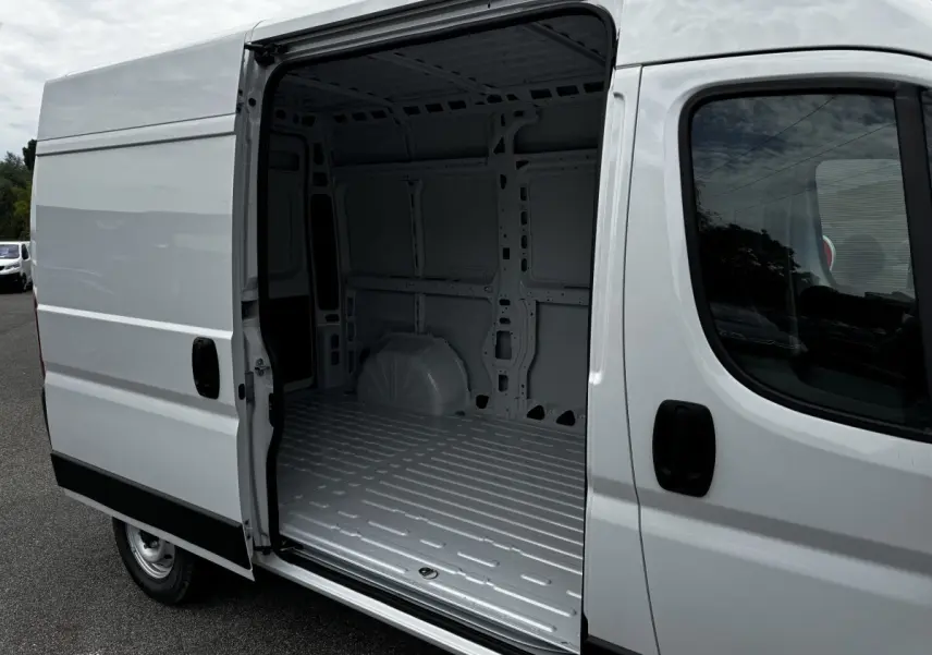 Vue 3/4 avant droit du Peugeot Boxer Fourgon blanc avec porte latérale coulissante ouverte montrant l’espace de chargement vide.