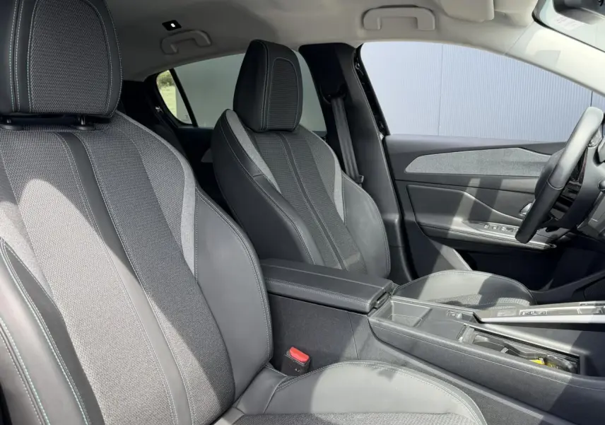 Vue intérieure côté gauche des sièges avant gris foncé avec surpiqûres bleues et accoudoir central de la Peugeot 308 Hybrid 2025.