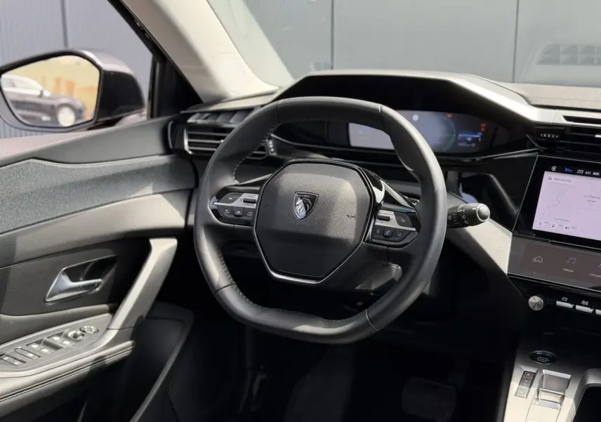 Vue intérieure centrée sur le volant cuir noir de la Peugeot 308 Hybrid 2025 avec écran tactile et commandes intégrées.