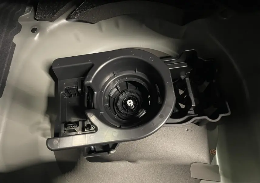 Gros plan sur le compartiment de rangement du kit de dépannage pneumatique dans le coffre d’une Peugeot 208 noire métallisée.