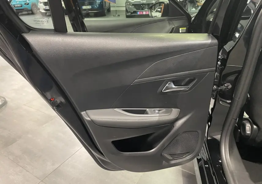 Porte arrière gauche ouverte de Peugeot 208 noire métallisée, montrant la garniture intérieure avec commande de vitre et haut-parleur.
