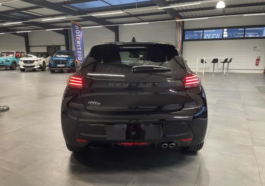 Vue arrière d'une Peugeot 208 noire métallisée hybride, avec feux arrière allumés et double sortie d'échappement chrome.