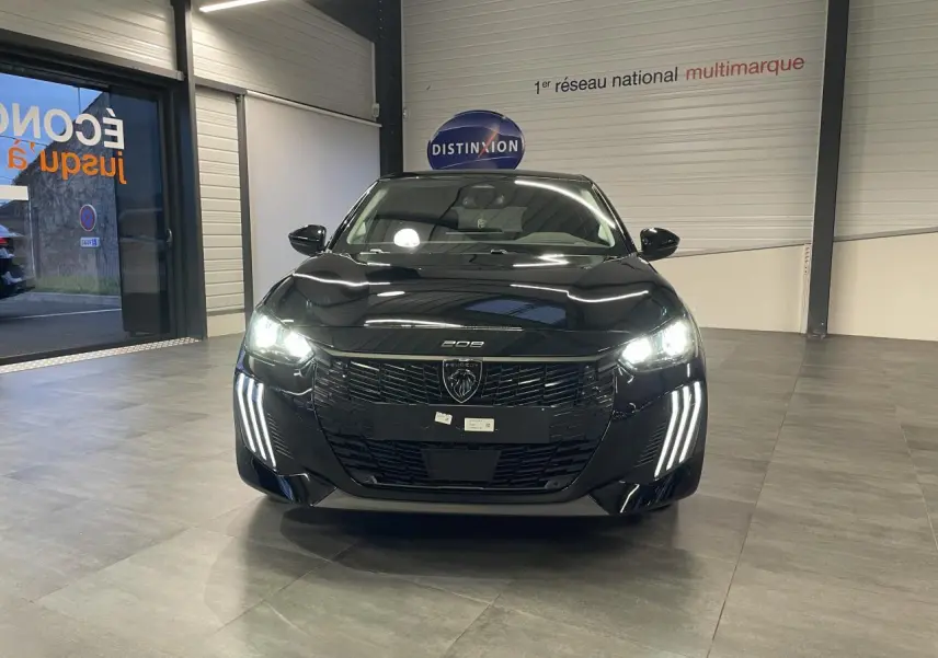 Vue avant d'une Peugeot 208 noire métallisée avec phares et feux diurnes LED allumés en intérieur showroom.
