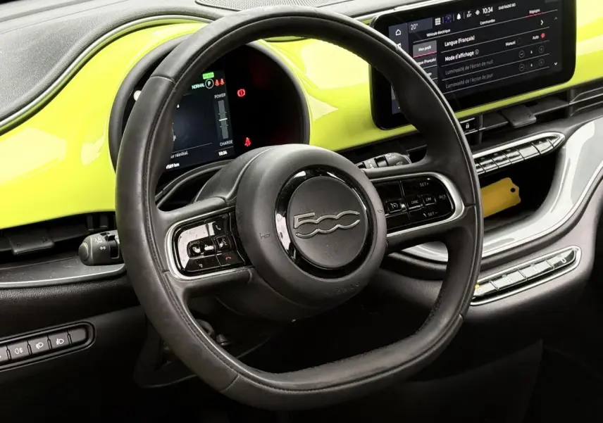 Vue intérieure centrée sur le volant noir et le tableau de bord jaune acid d'une Fiat 500 électrique 2024.