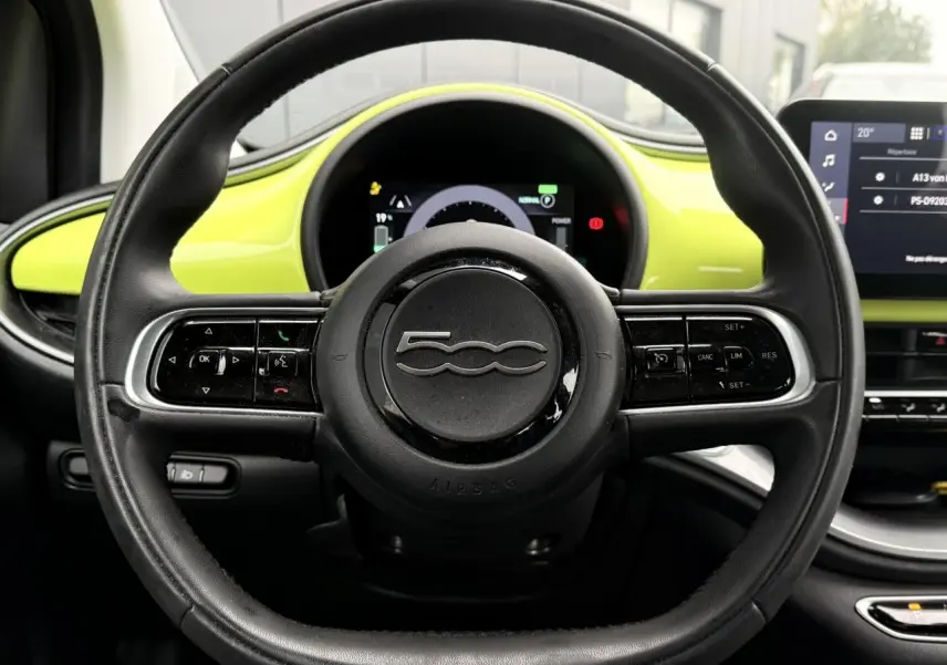 Vue centrée sur le volant noir de la Fiat 500 électrique 2024, avec tableau de bord et garniture jaune Acid en arrière-plan.