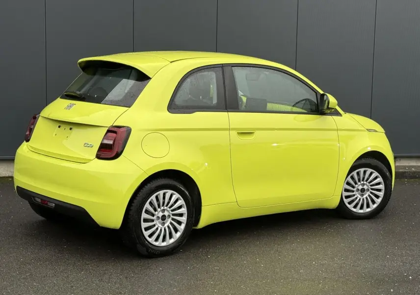 Fiat 500 électrique jaune Acid vue 3/4 arrière côté droit sur sol mouillé devant un mur gris.