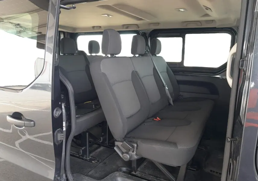 Vue intérieure côté droit du Renault Trafic Combi gris foncé, montrant les sièges passagers en tissu noir sur trois rangées.