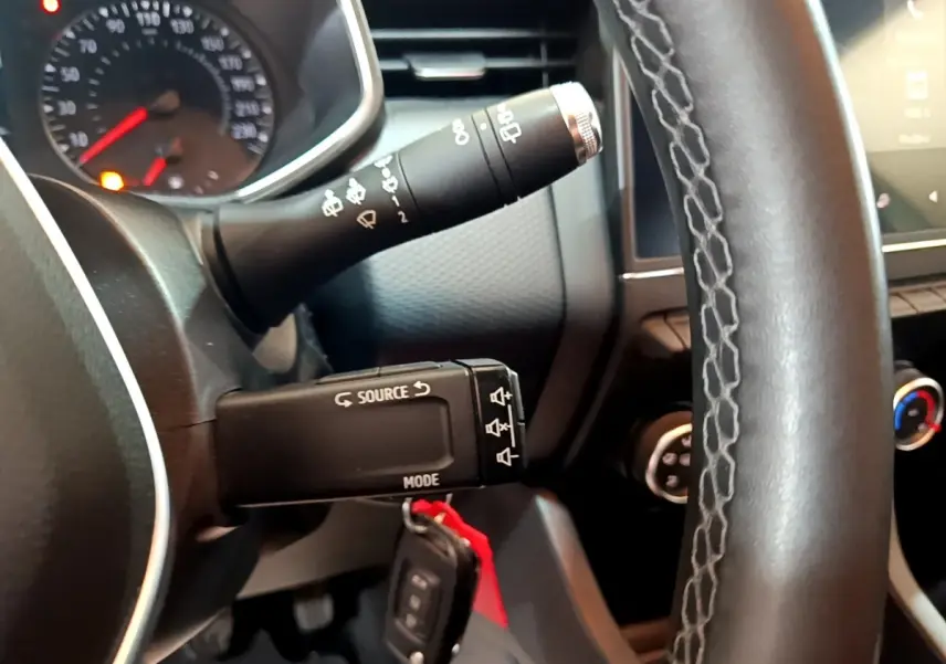 Gros plan sur le volant cuir et les commandes au volant d'une Renault Clio Business blanche, tableau de bord partiellement visible.