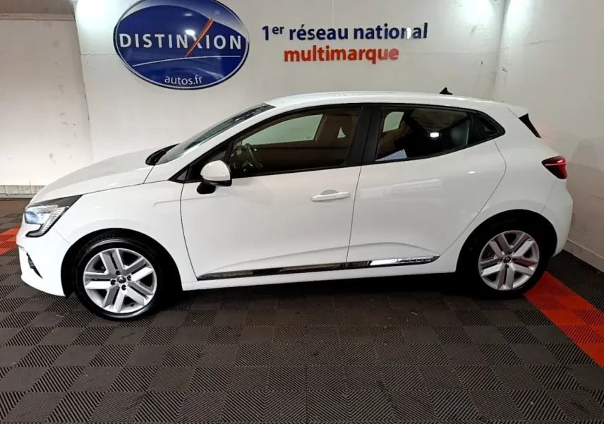 Profil côté gauche d'une Renault Clio Business TCe 100 blanche, avec jantes alliage et feux arrière allumés, en intérieur showroom.