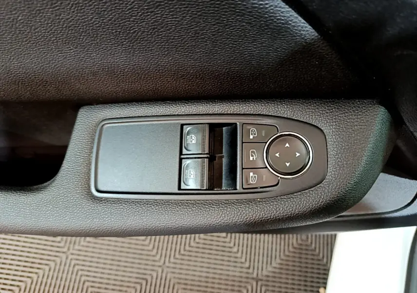 Gros plan sur les commandes de lève-vitres et réglage des rétroviseurs côté conducteur d'une Renault Clio blanche 2019.