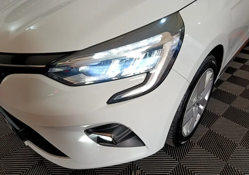 Gros plan sur l'avant droit blanc d'une Renault Clio 2019, mettant en valeur le phare LED allumé et la jante alu.