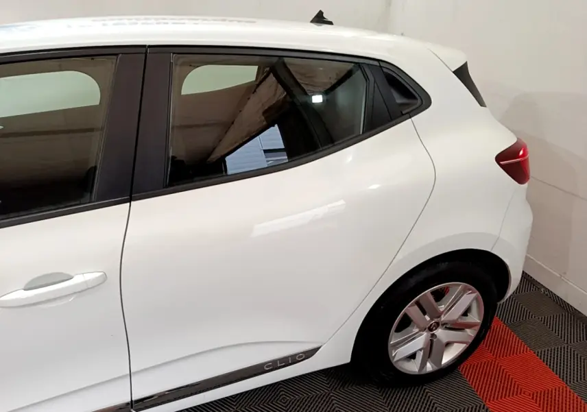 Vue latérale côté droit d'une Renault Clio blanche avec jante alliage et logo Clio sur la bas de porte.