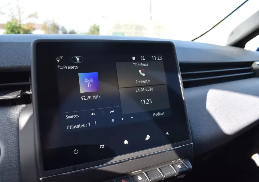 Écran tactile central de la Renault Clio V noir, affichant la radio FM et la connexion téléphone, vue intérieure avant.