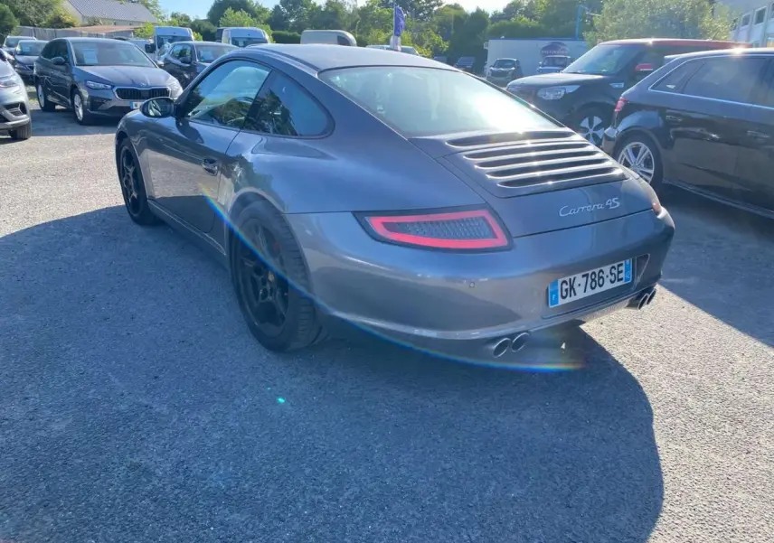 Vue 3/4 arrière droite d'une Porsche 911 Carrera 4S gris météore avec jantes noires et double sortie d'échappement.