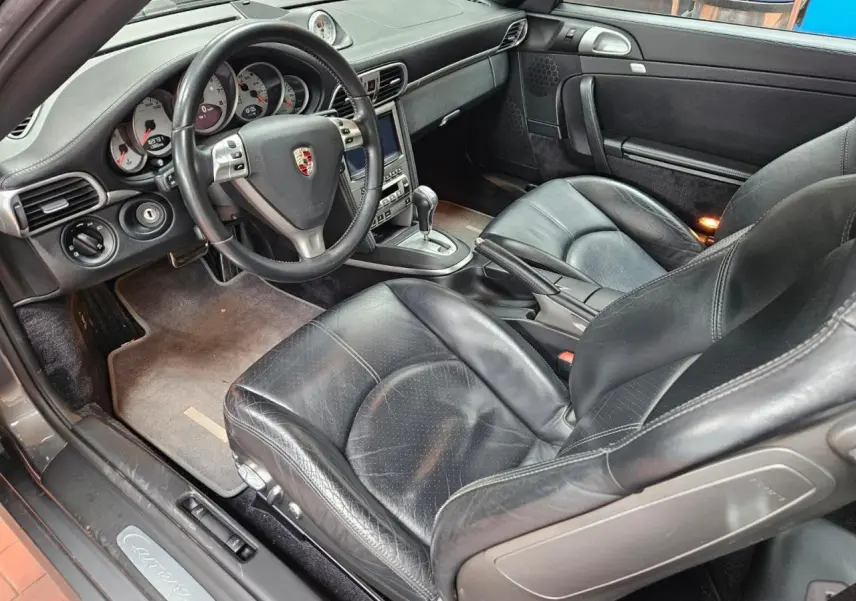 Vue intérieure côté conducteur de la Porsche 911 Carrera 4S 2007 avec sièges sport cuir noir et volant multifonction.