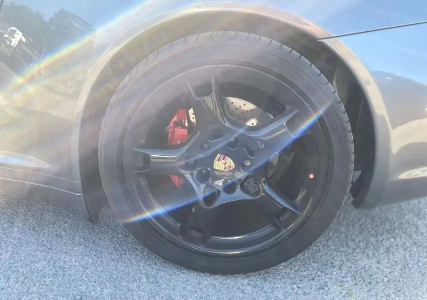 Gros plan sur la jante noire Carrera Sport 19 pouces avec étrier de frein rouge sur Porsche 911 gris météore côté arrière droit.