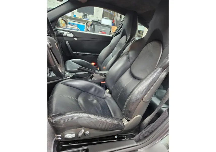 Vue intérieure côté conducteur de la Porsche 911 Carrera 4S 2007 avec sièges sport cuir noir et volant multifonction.