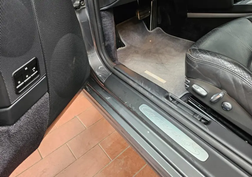 Vue intérieure côté conducteur de la Porsche 911 Carrera 4S 2007 gris météore, siège cuir noir et seuil de porte Carrera 4S.