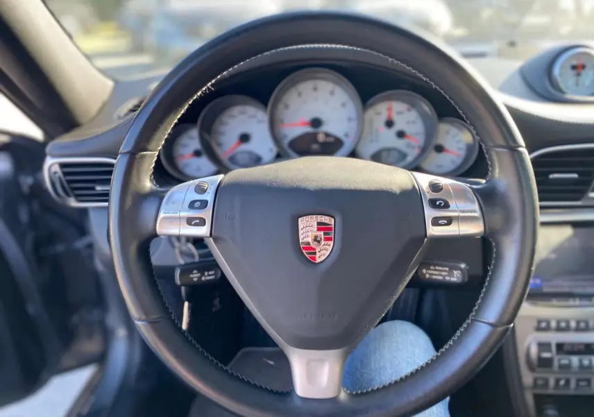 Vue rapprochée du volant en cuir noir avec logo Porsche et compteurs blancs d'une 911 Carrera 4S 2007.