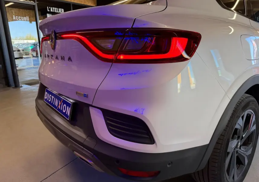 Vue 3/4 arrière droite d'un Renault Arkana blanc nacré avec feux LED allumés et jantes alu noires.